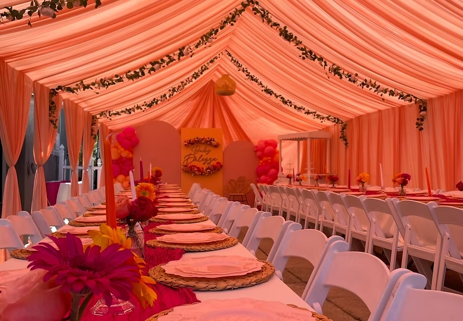 A peach-draped tent with white folding chairs and floral table settings at a baby shower styled by Duran Events Rentals & Decor