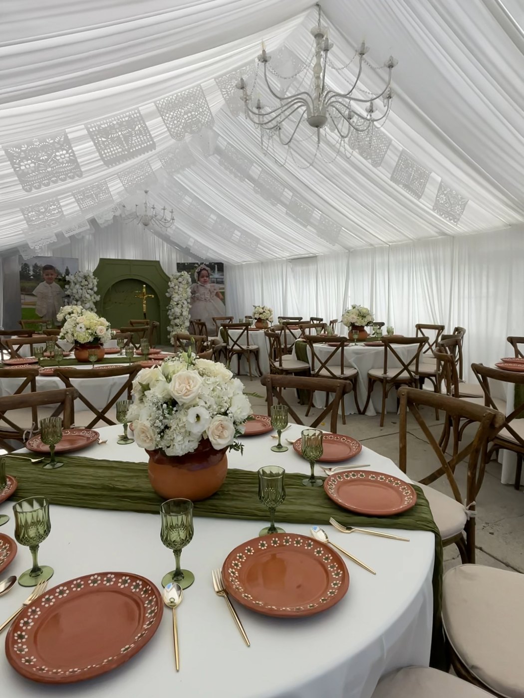 Christening celebration under a white tent with papel picado banners, cross-back chairs, terracotta talavera plates and green table runners